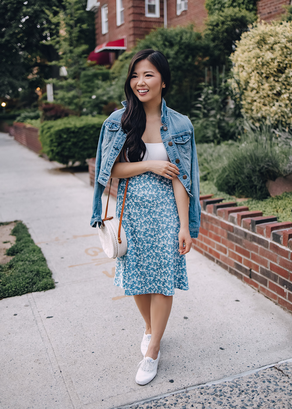 Casual Spring Outfit for Women: Denim Jacket, White Bodysuit, Blue Floral Midi Skirt, White Straw Circle Bag, White Leather Sneakers