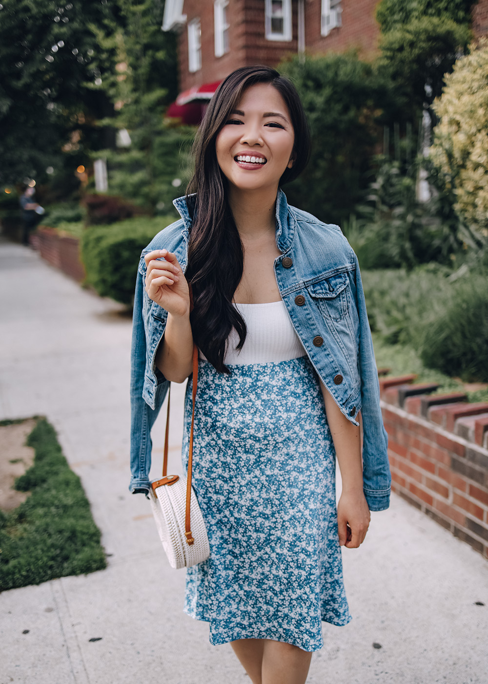 Casual Spring Outfit for Women: Denim Jacket, White Bodysuit, Blue Floral Midi Skirt, White Straw Circle Bag, White Leather Sneakers